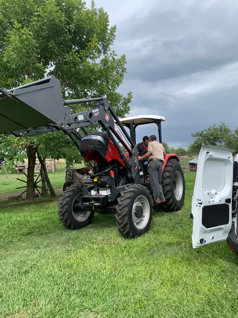 Operarios de Casa Vale sobre un tractor con pala frontal en el campo del cliente, junto al utilitario del taller